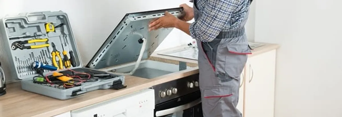 Cooktop repair technician lifting a built-in stovetop for service in Pueblo, CO