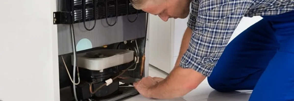Refrigerator repair technician servicing the compressor and condenser area in Pueblo, CO