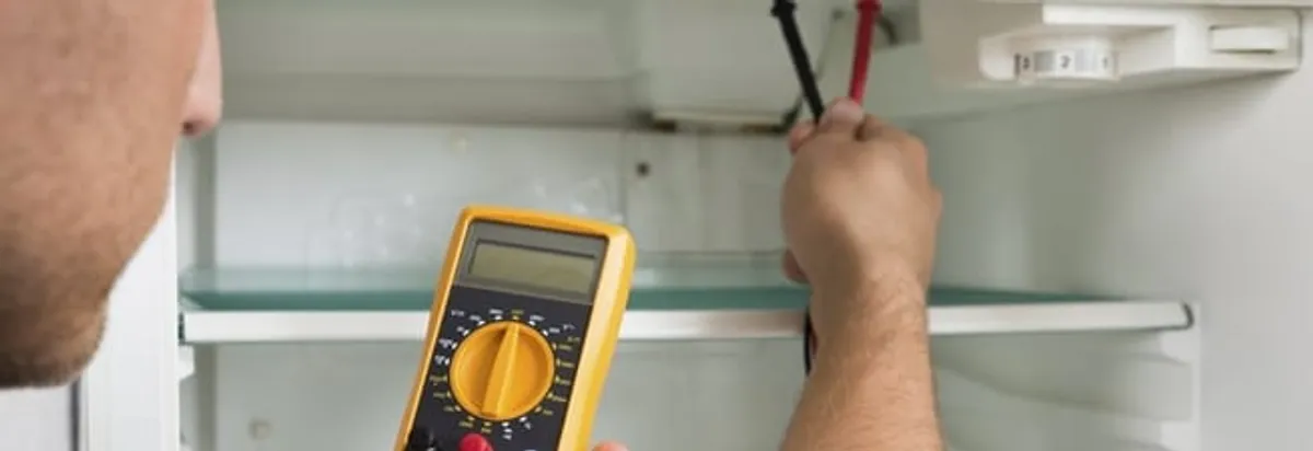 Refrigerator repair technician testing electrical components with a multimeter in Pueblo, CO